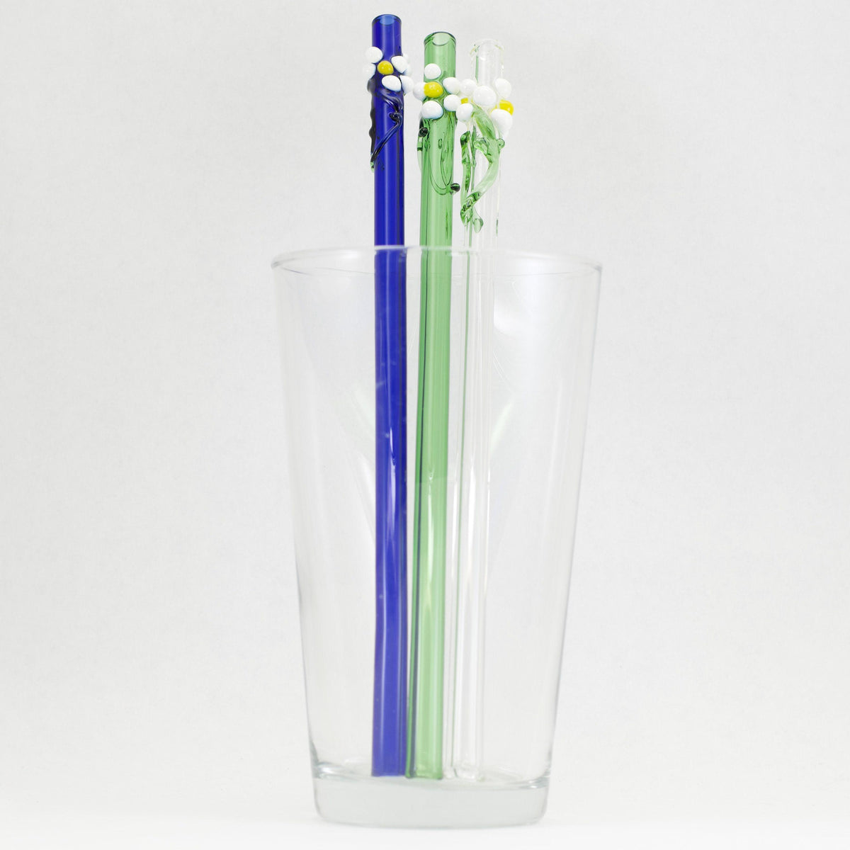 Clear glass glass with blue and green straws inside on a white background