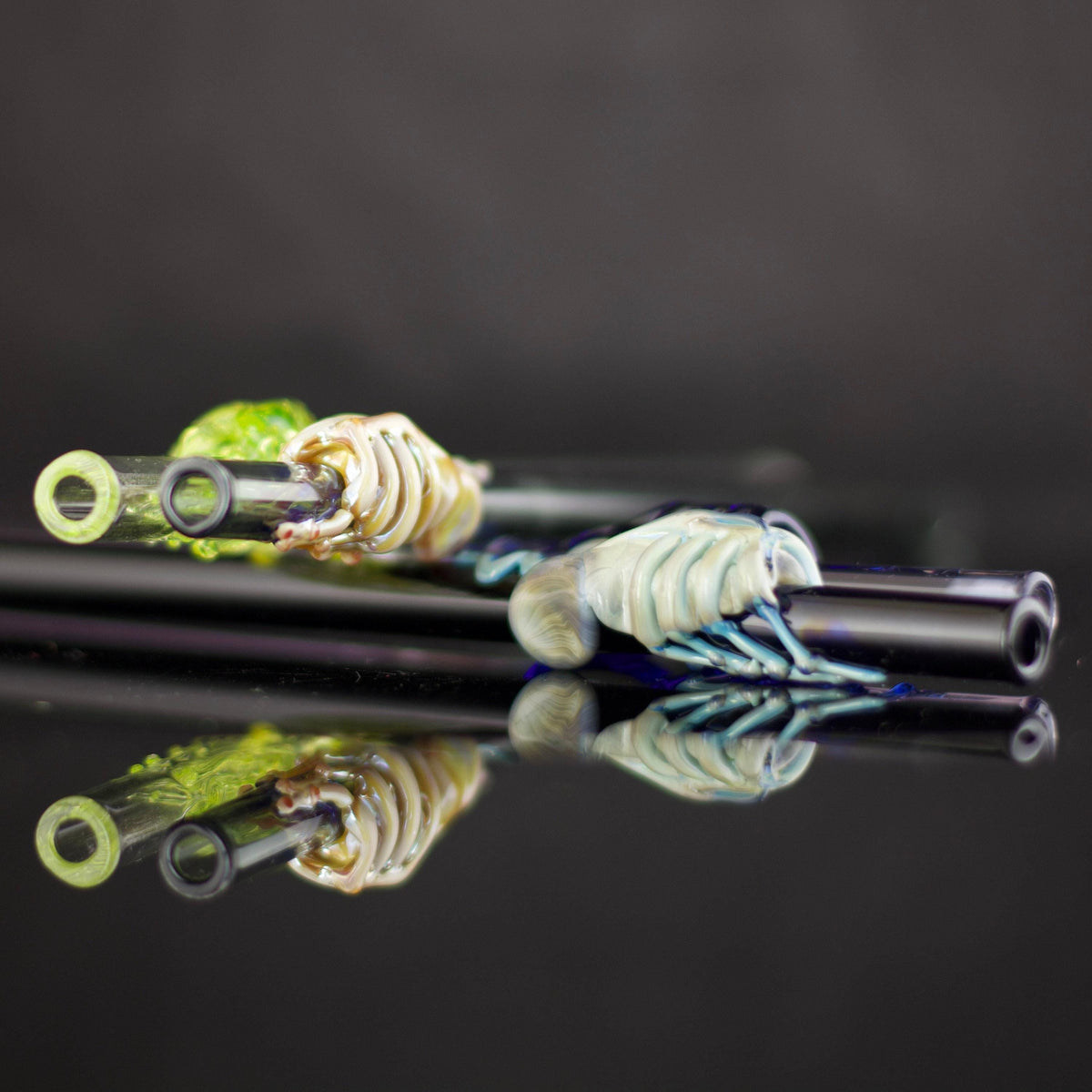 Glass straws with decorative elements on a reflective surface