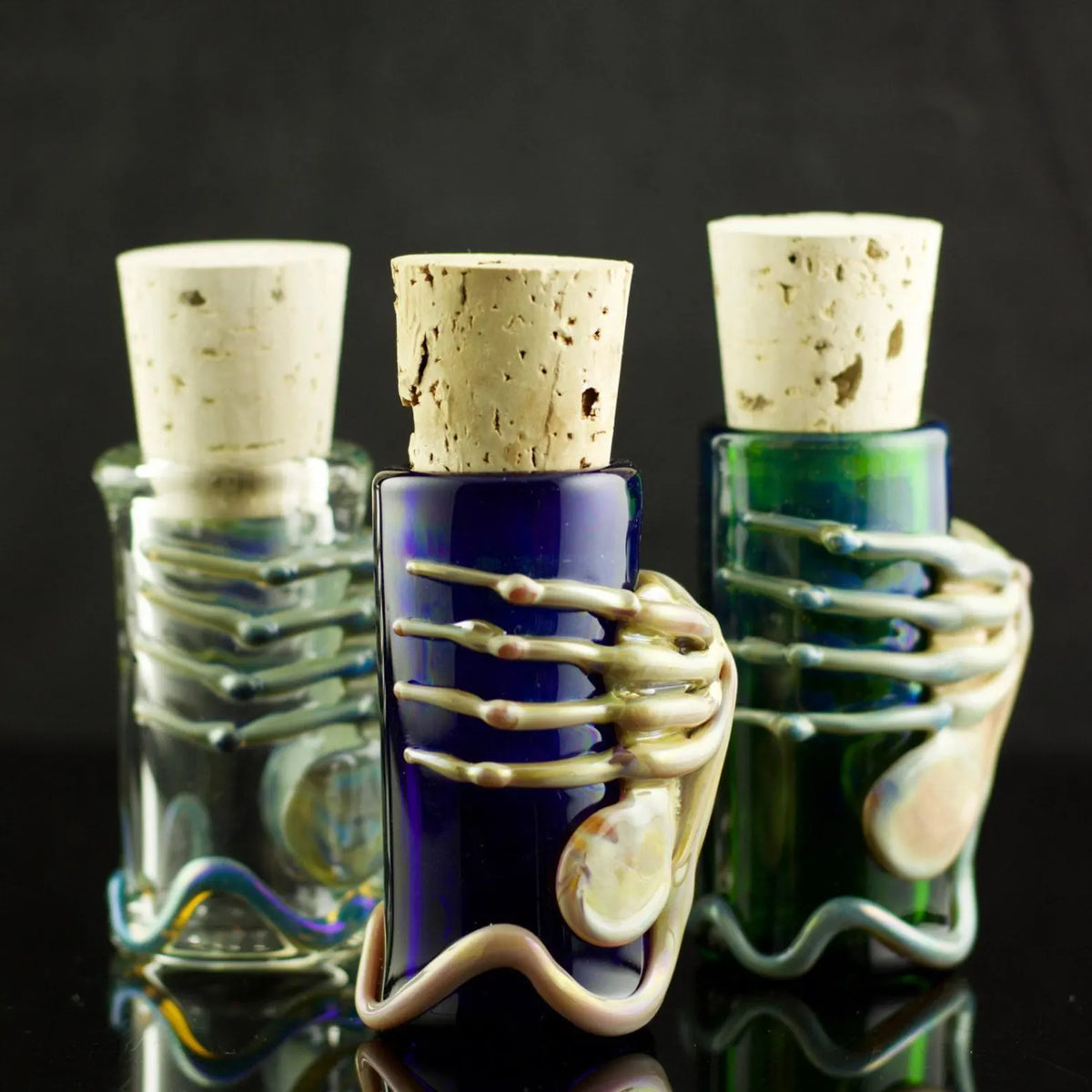 Three glass bottles with cork stoppers on a reflective surface against a dark background