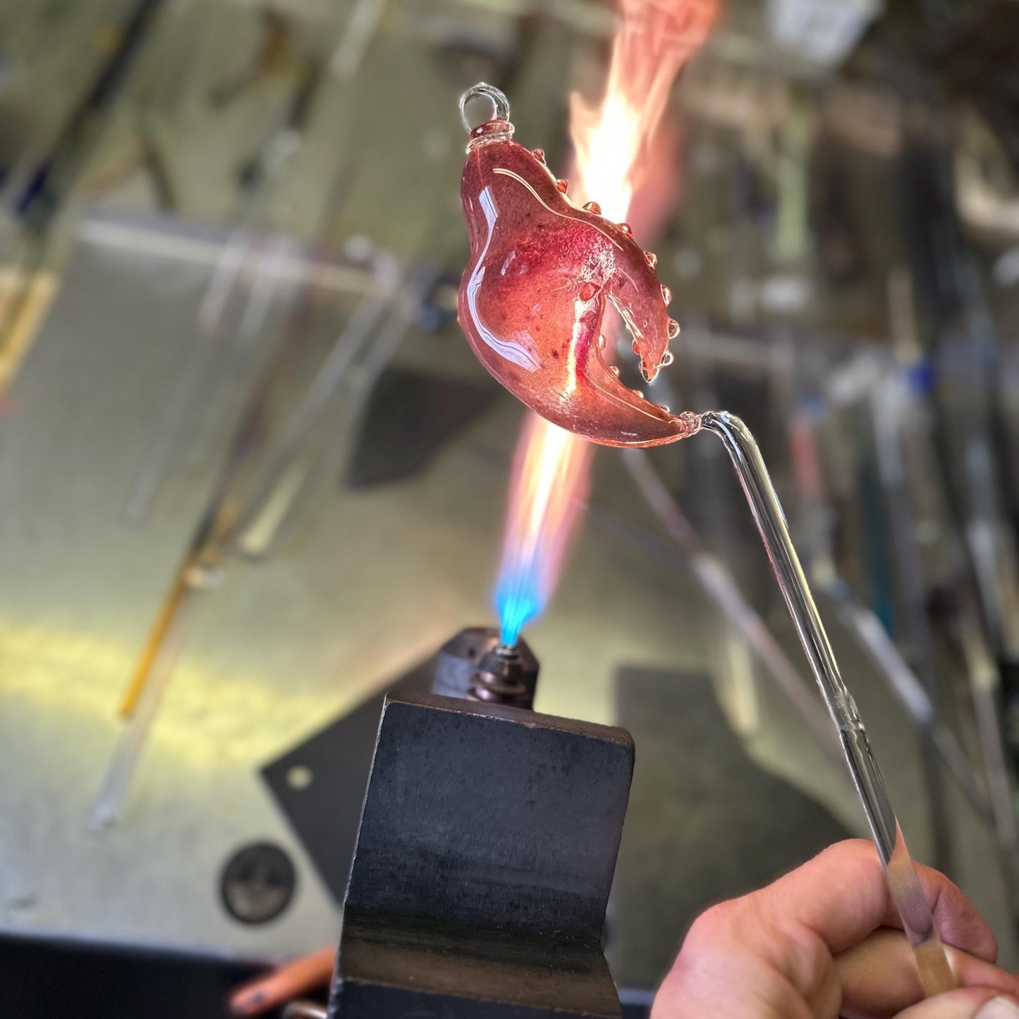 Glassblowing process with molten glass being shaped over a flame.