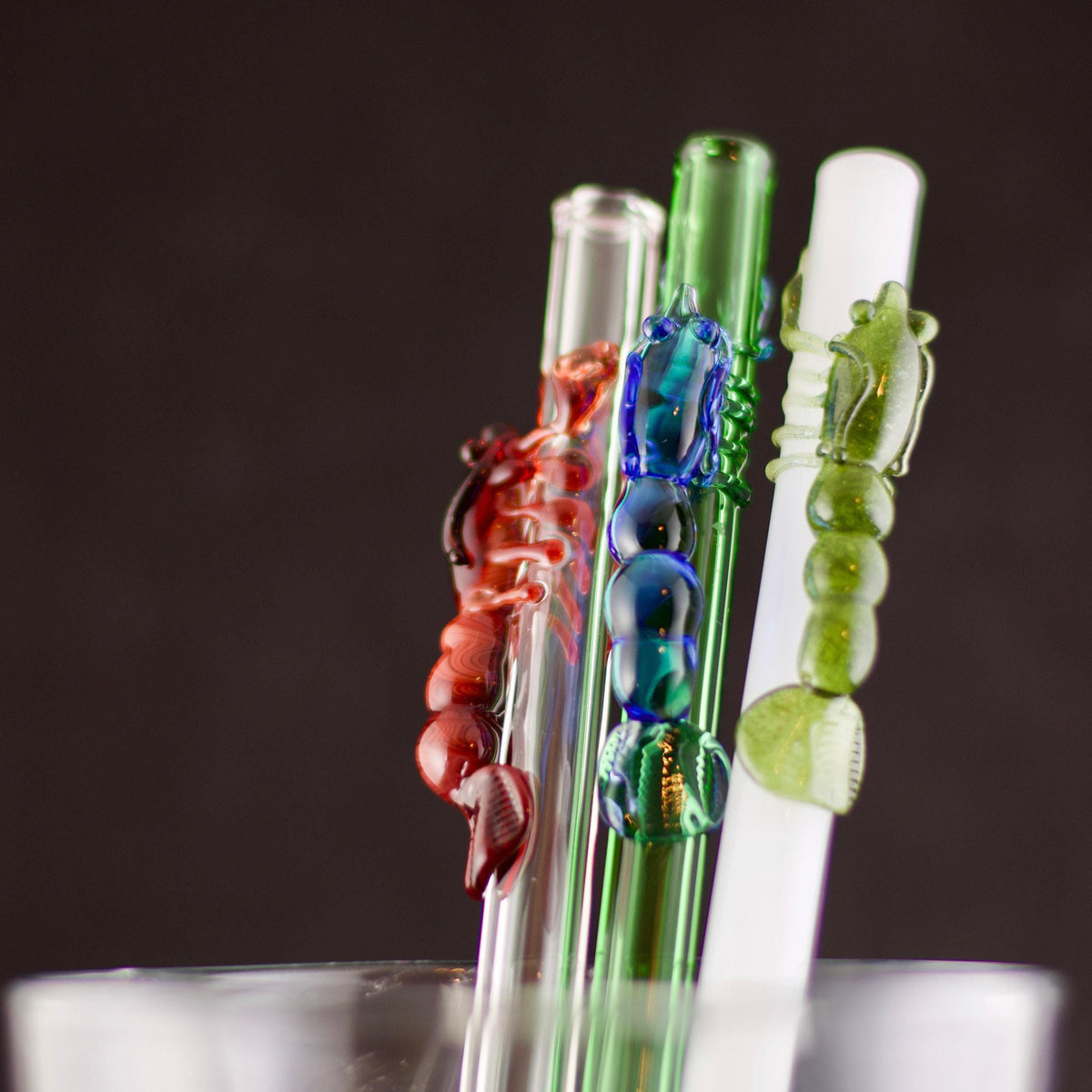 Three glass straw with colorful lobster designs on a dark background