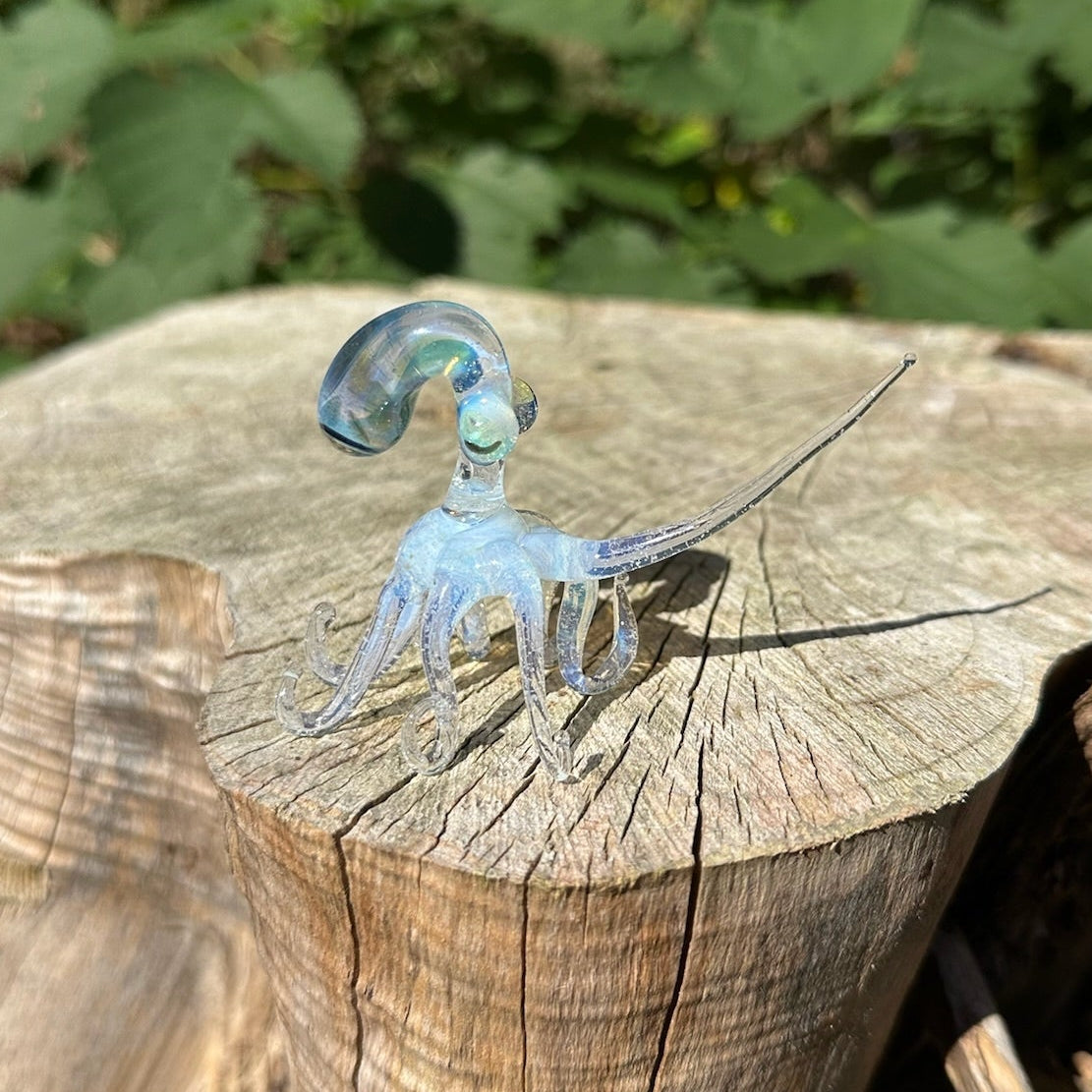 Secret white octopus figurine with leg stretched atop a wood stump. 