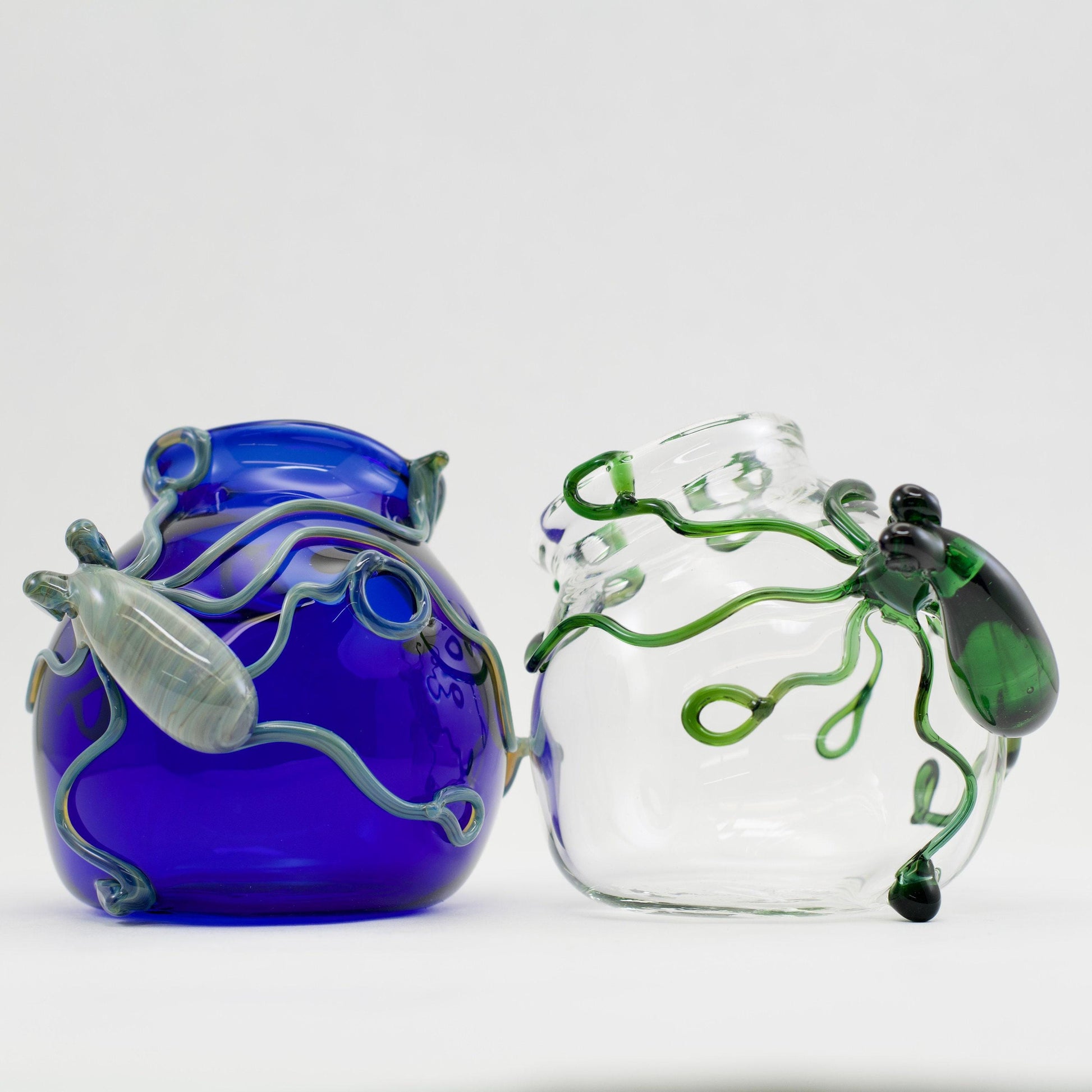 Two glass vases, one blue and one clear with green designs, on a white background