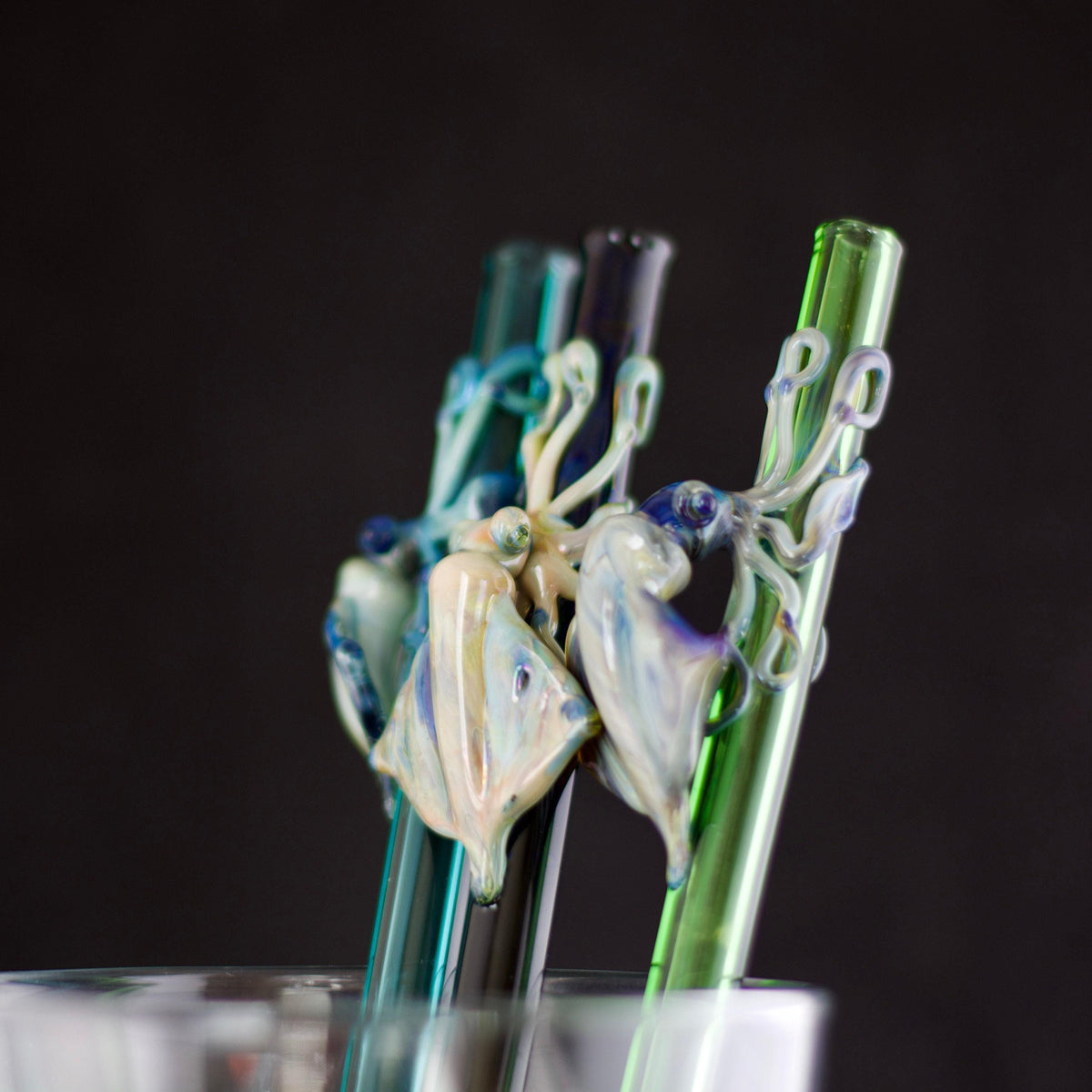 Three glass straws with decorative ends on a black background